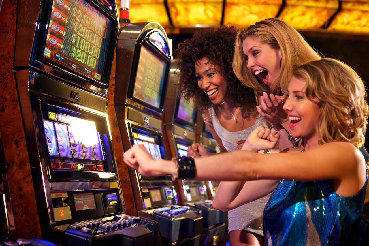 Three women in dresses excited over a slot machine.