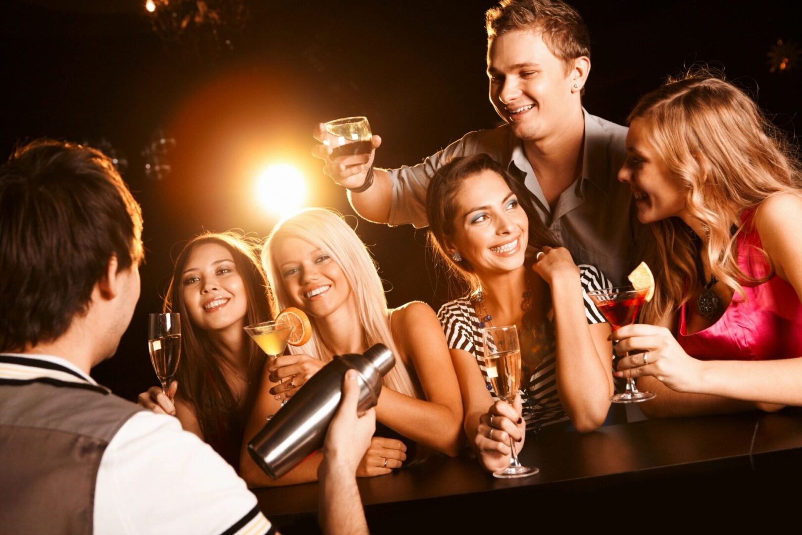 A bartender mixing up cocktails in front of a bunch of women with drinks.