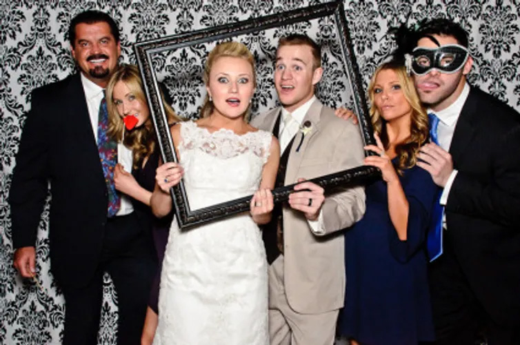 A group of people in dress clothes, holding a picture frame and posing for wedding photo.